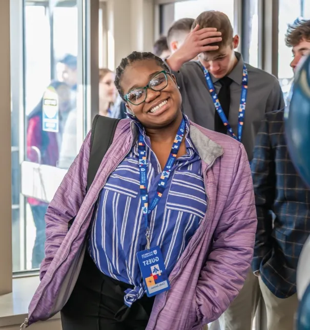 One female student walking into an event indoors, smiling.